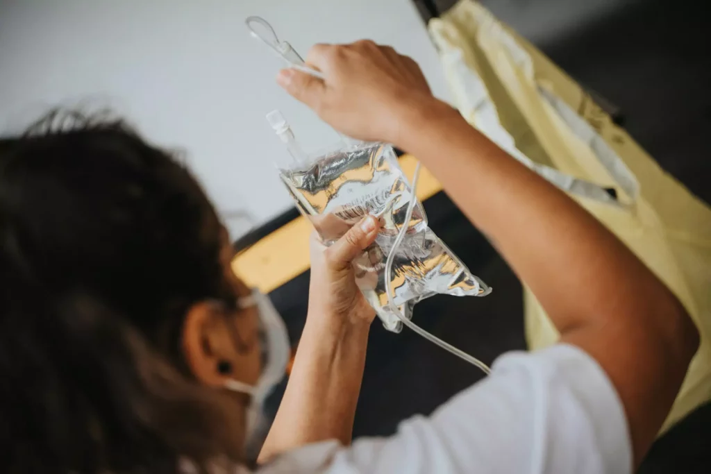 A woman holds up a bad of fluids, connecting them to an IV drip.