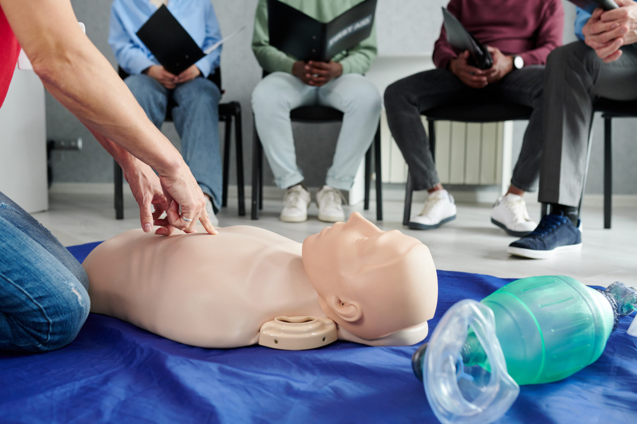 Close-up of female instructor using mannequin on floor to teach cardiopulmonary resuscitation at training class
