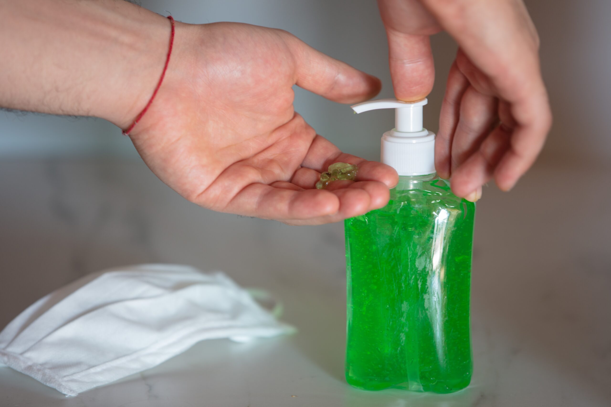 A closeup of a person using liquid soap on the table near a face mask - coronavirus concept