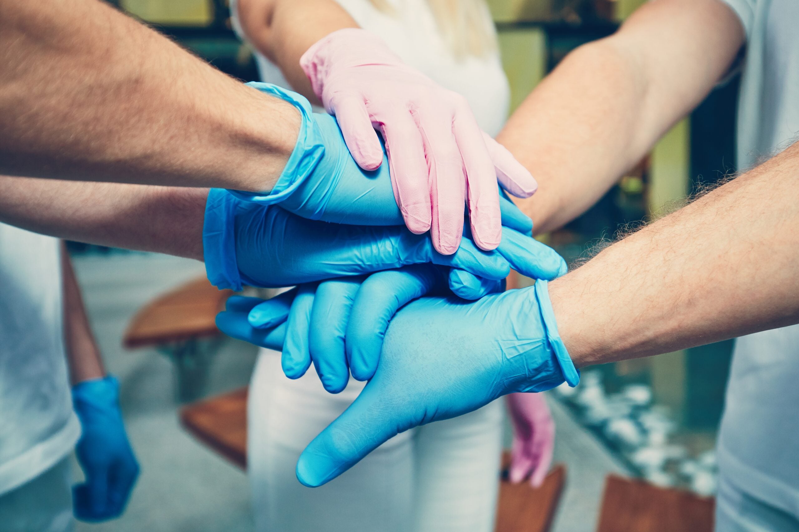 Teamwork of the doctors in hospital. Hands of four men in blue gloves and one woman in pink gloves. Themes health care, cooperation, trust and success.
