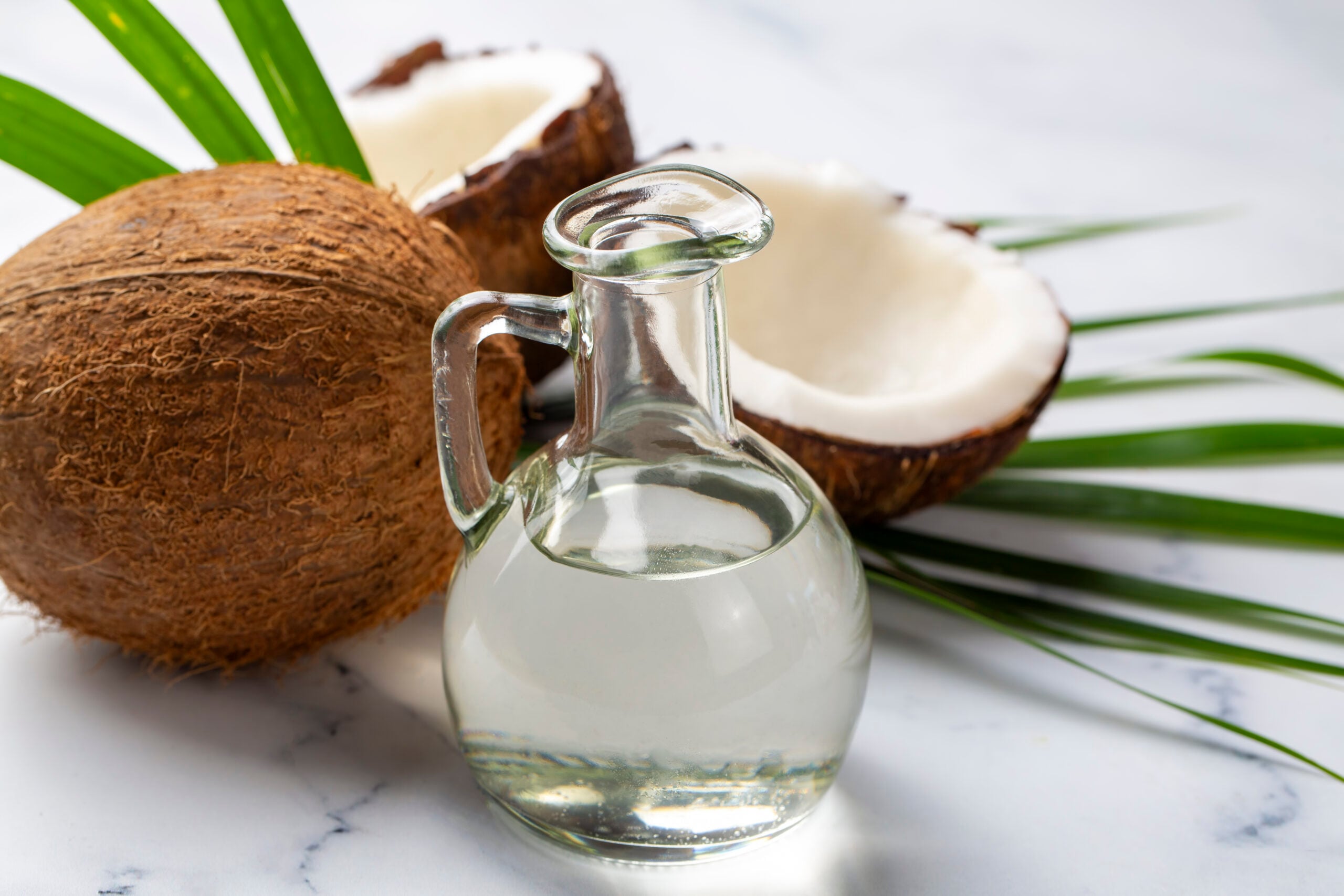Bottle of coconut oil and fresh coconuts with palm leaf