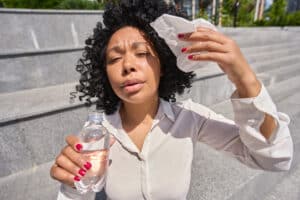 Multiracial woman sitting in the heatstroke wiping herself with a napkin and drinking water