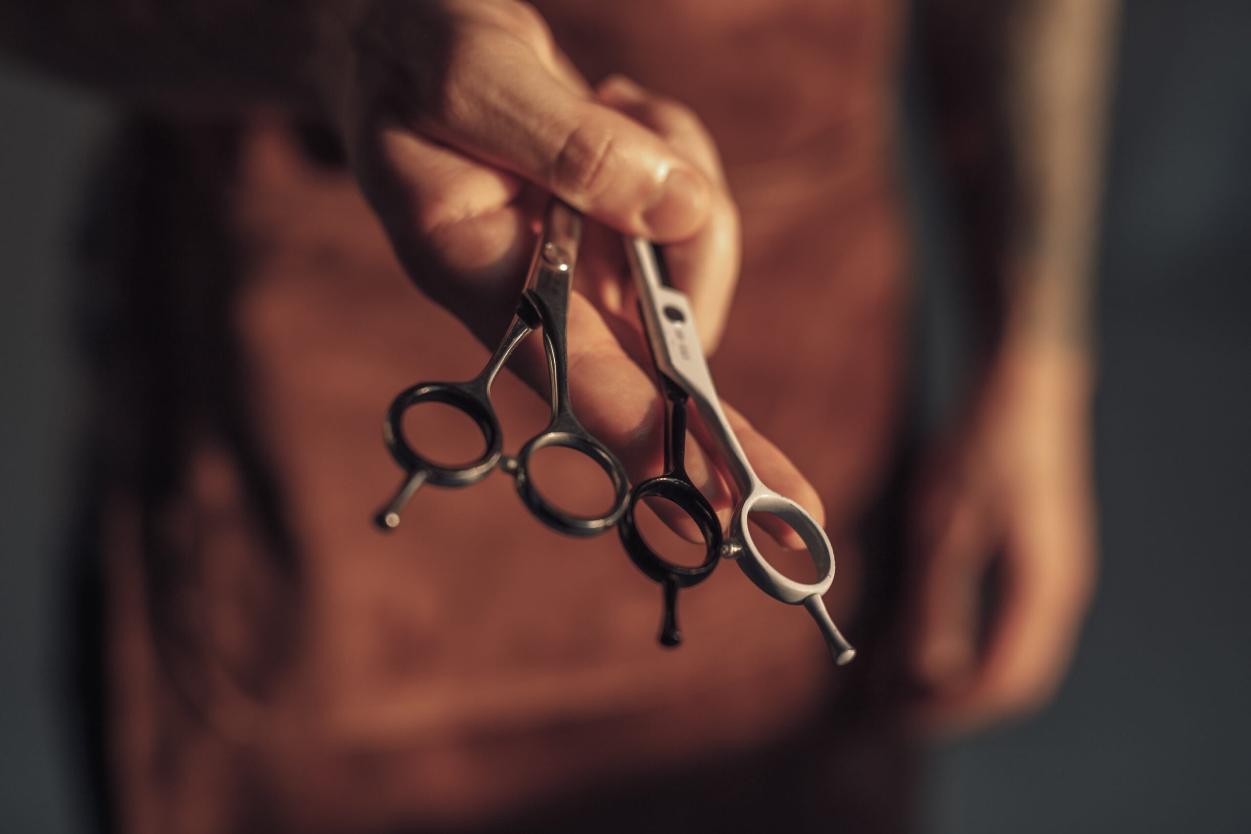 Closeup anonymous hairdresser showing professional sharp scissors to camera while working in salon