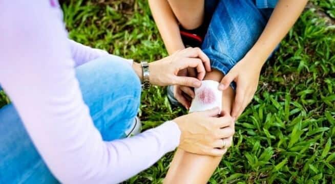 mother placing bandage on child's scraped knee