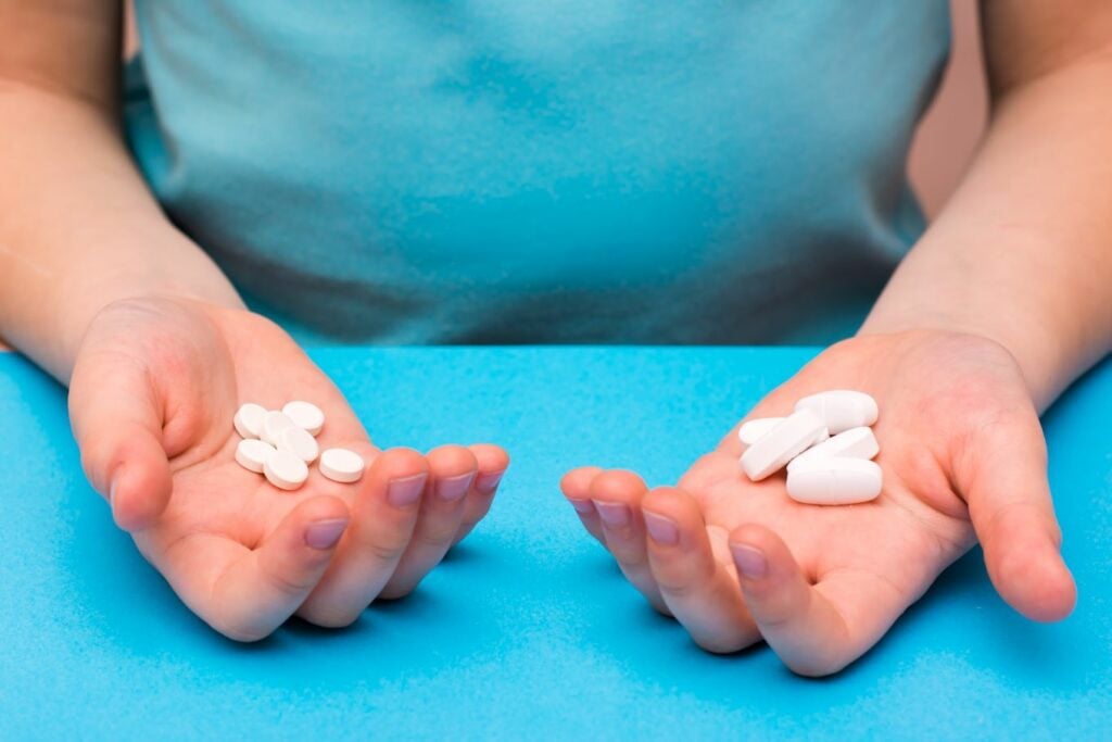 Paracetamol vs Ibuprofen. - person holding pills in either hands