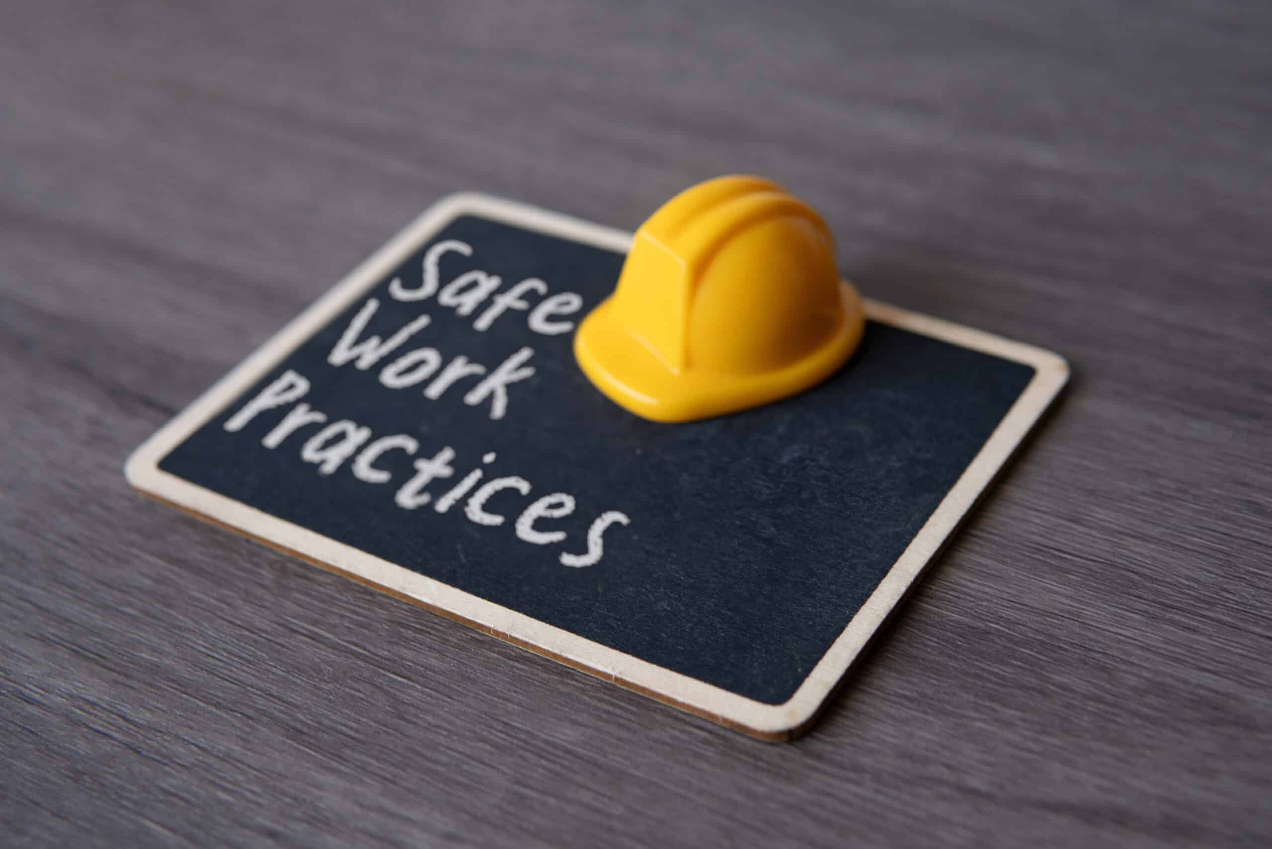 Small chalkboard with the text &ldquo;Safe Work Practices&rdquo; and yellow hard hat. Concepts of safety, precaution, and standards in the workplace.