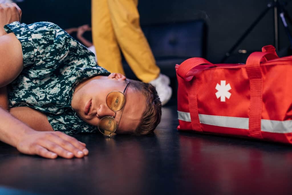 RECOVERY POSITION FOR - man in sunglasses lying on floor near first aid kit bag in nightclub