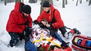 Hypothermia - Paramedics from mountain rescue service provide operation outdoors in winter in forest, injured person in stretcher.