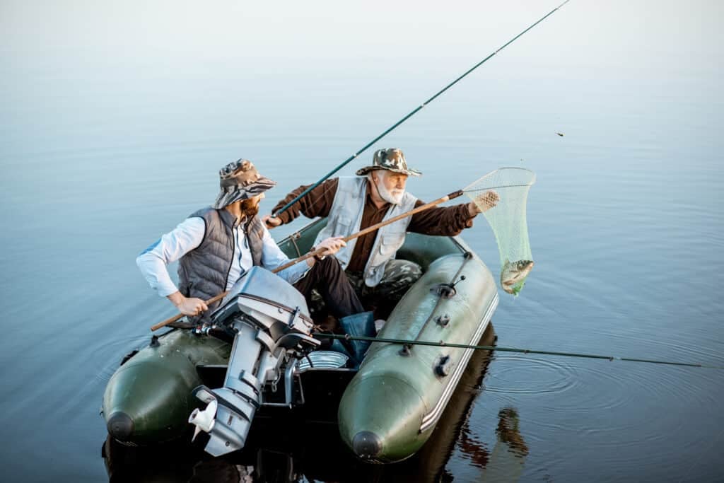Grandfather with adult son fishing on the inflatable boat on the lake early in the morning