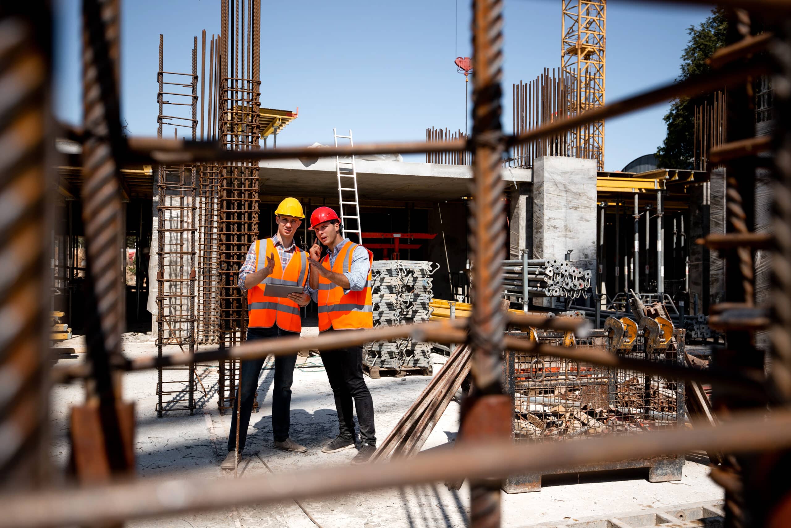 white card jobs - construction workers in orange work vests and helmets discuss a building project on the open air building site with a lot of steel frames . .