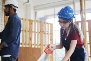 World Youth Skills Day 2026 - Side view portrait of modern female carpenter measuring wooden part making furniture over working table in workshop