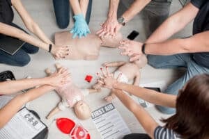World First Aid Day - Group of people learning how to make first aid heart compressions with dummies during the training indoors