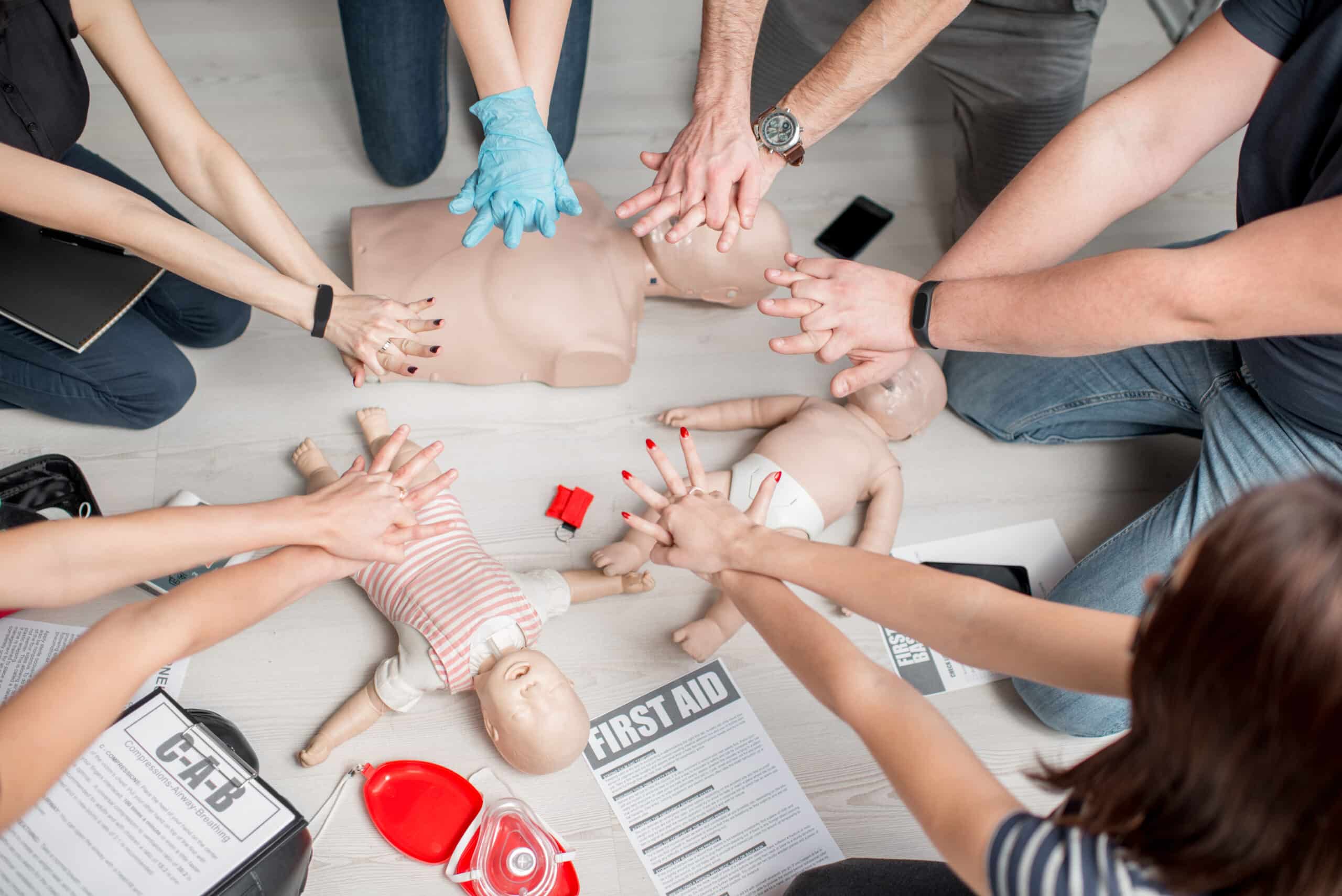 World First Aid Day - Group of people learning how to make first aid heart compressions with dummies during the training indoors