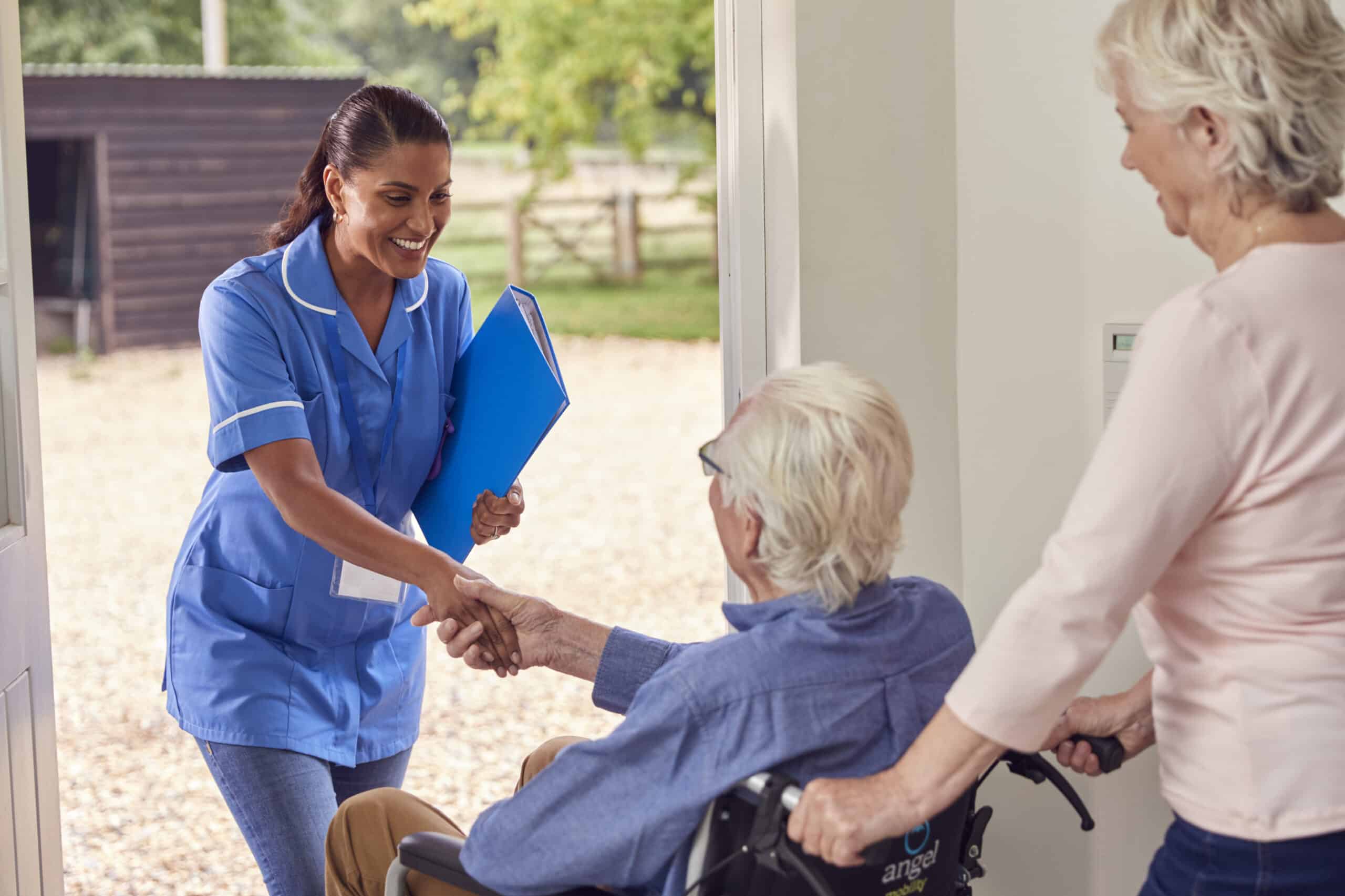 World Senior Citizens Day - 2026 - Senior Couple With Man In Wheelchair Greeting Female Nurse Or Care Worker Making Home Visit At Door-