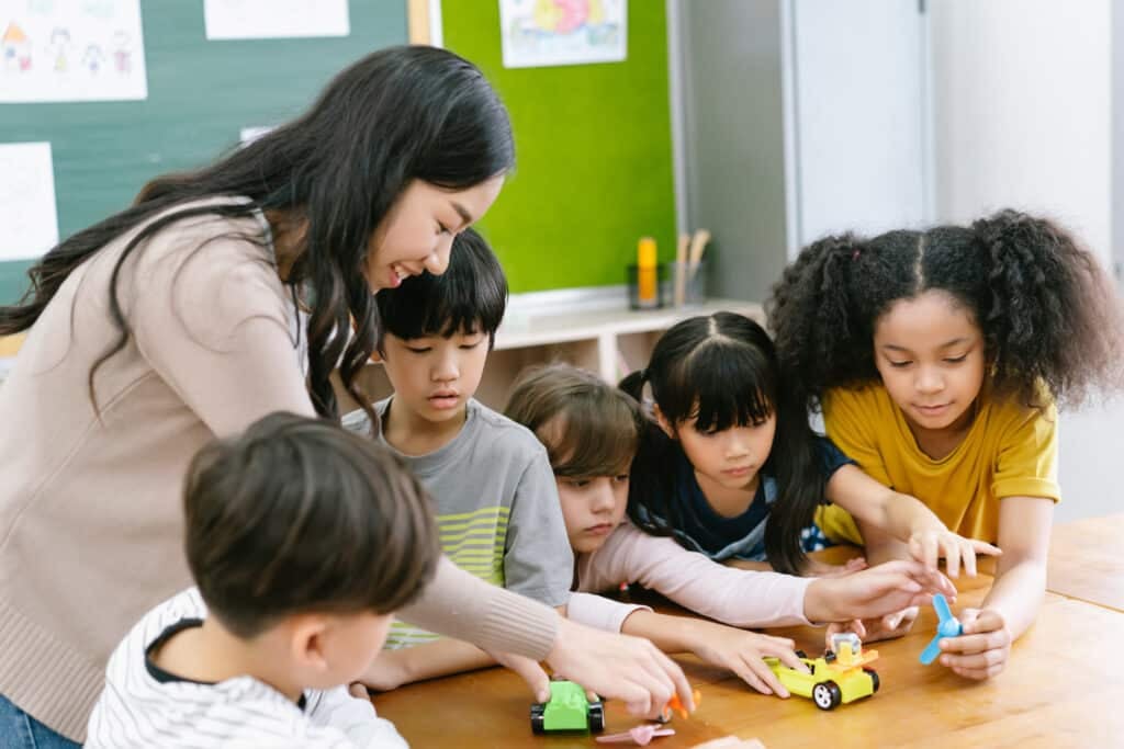 Early Childhood Education - Group of Diverse Elementary School Pupils and Female Asian teacher demonstrating making electric remote control car in science lesson. Education, elementary school, learning, science workshop concept.
