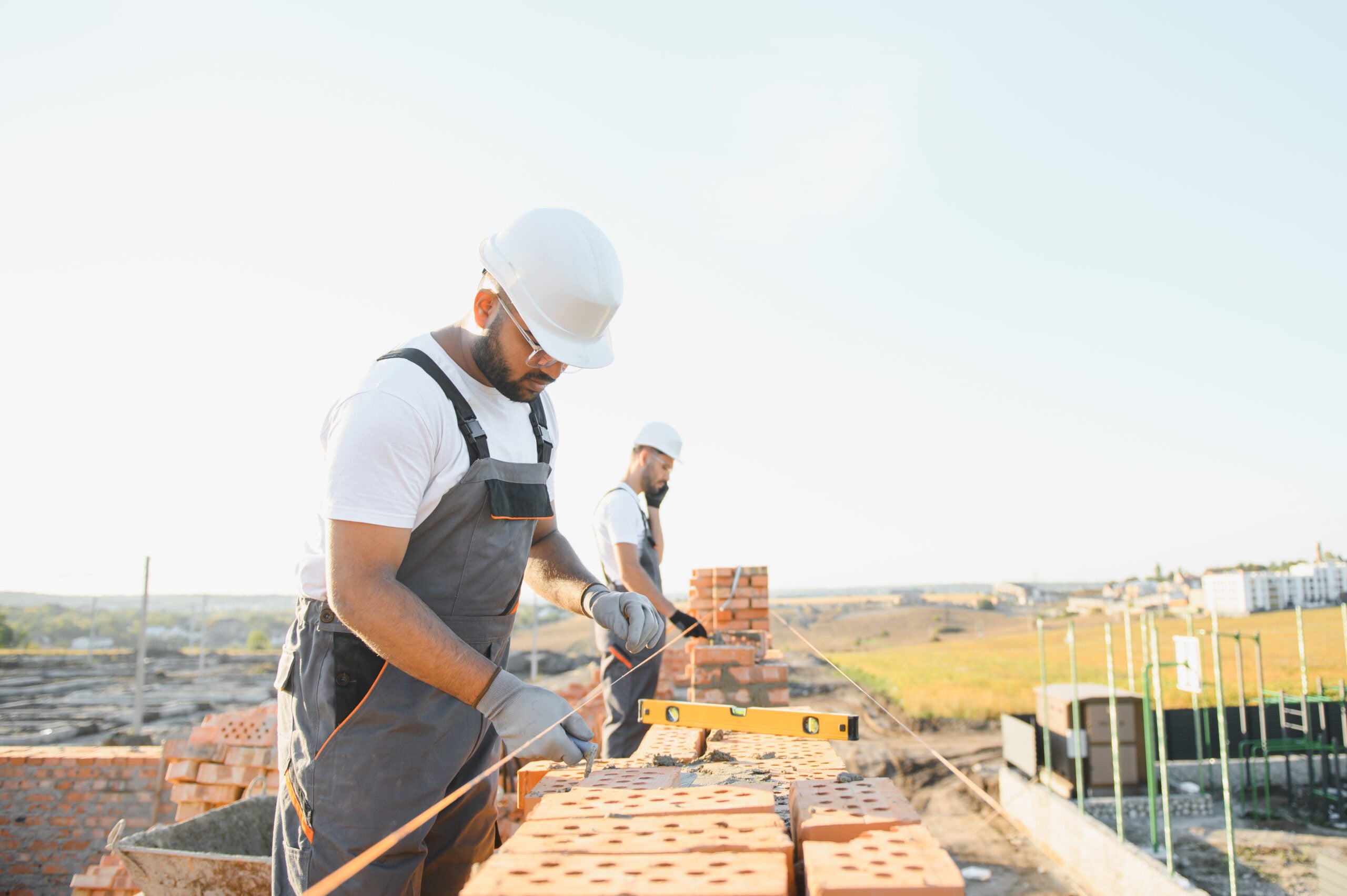 A team of Indian construction workers in overalls and hard hats are building a brick wall