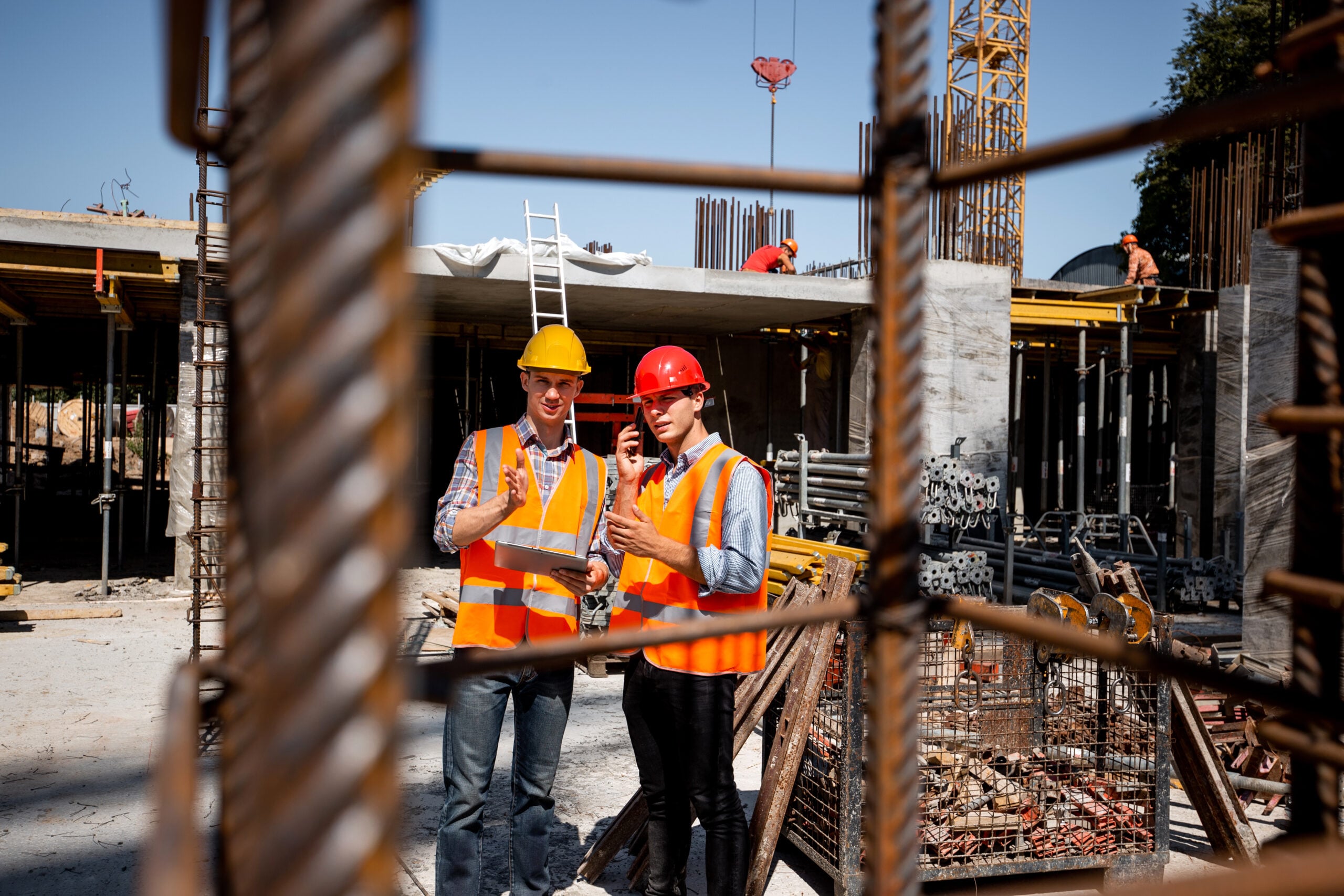 National Safe Work Month 2026 - Architect and structural engineer in orange work vests and helmets discuss a building project on the open air building site with a lot of steel frames