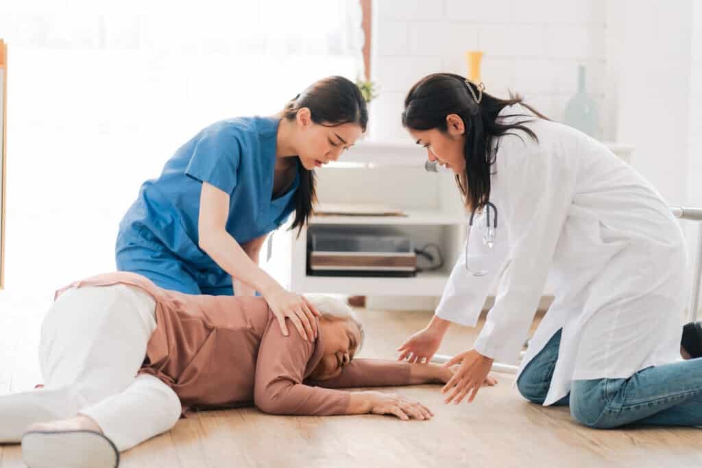 CPR - senior patient falling on the ground floor at home, Asian caregiver helping elderly older female from accident after doing physical therapy then rescued by attractive therapist nurse, health insurance