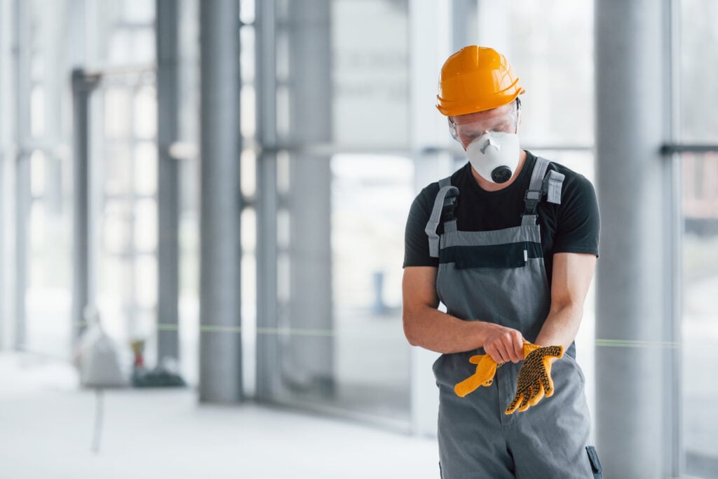 PPE - Man in grey uniform preparing for work indoors in modern big office at daytime.